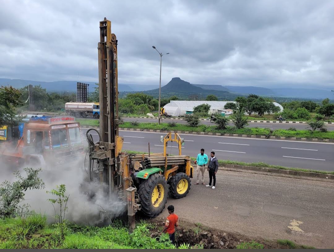 Tractor-mounted borewell rig drilling beside a highway near Satara
