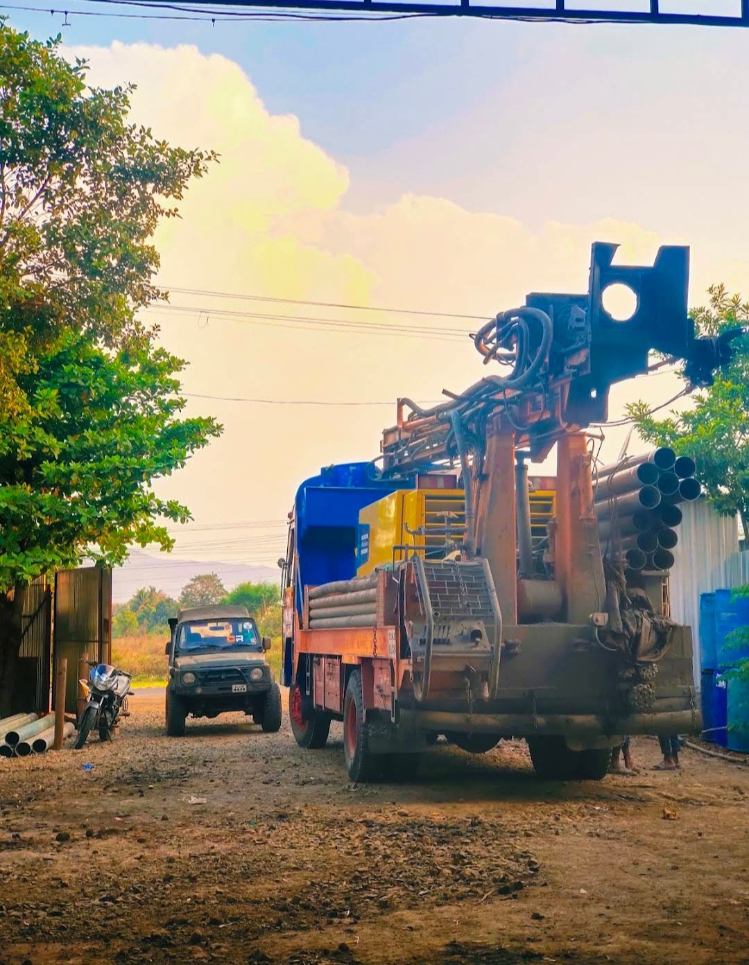 Truck-mounted borewell drilling rig loaded with casing pipes at evening